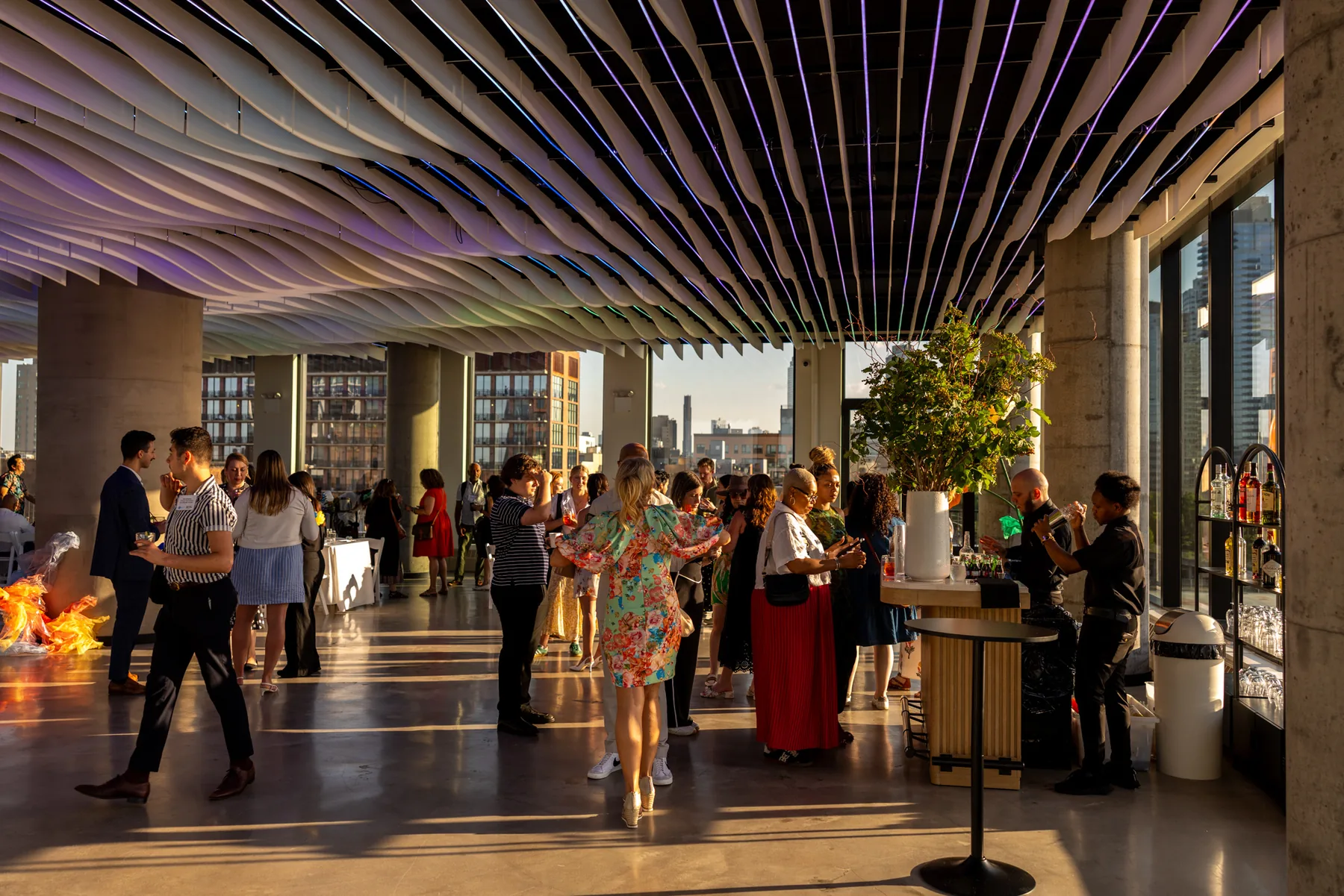 Corporate networking event under the sculptural wave ceiling at VESPER in Brooklyn with Manhattan skyline views at golden hour