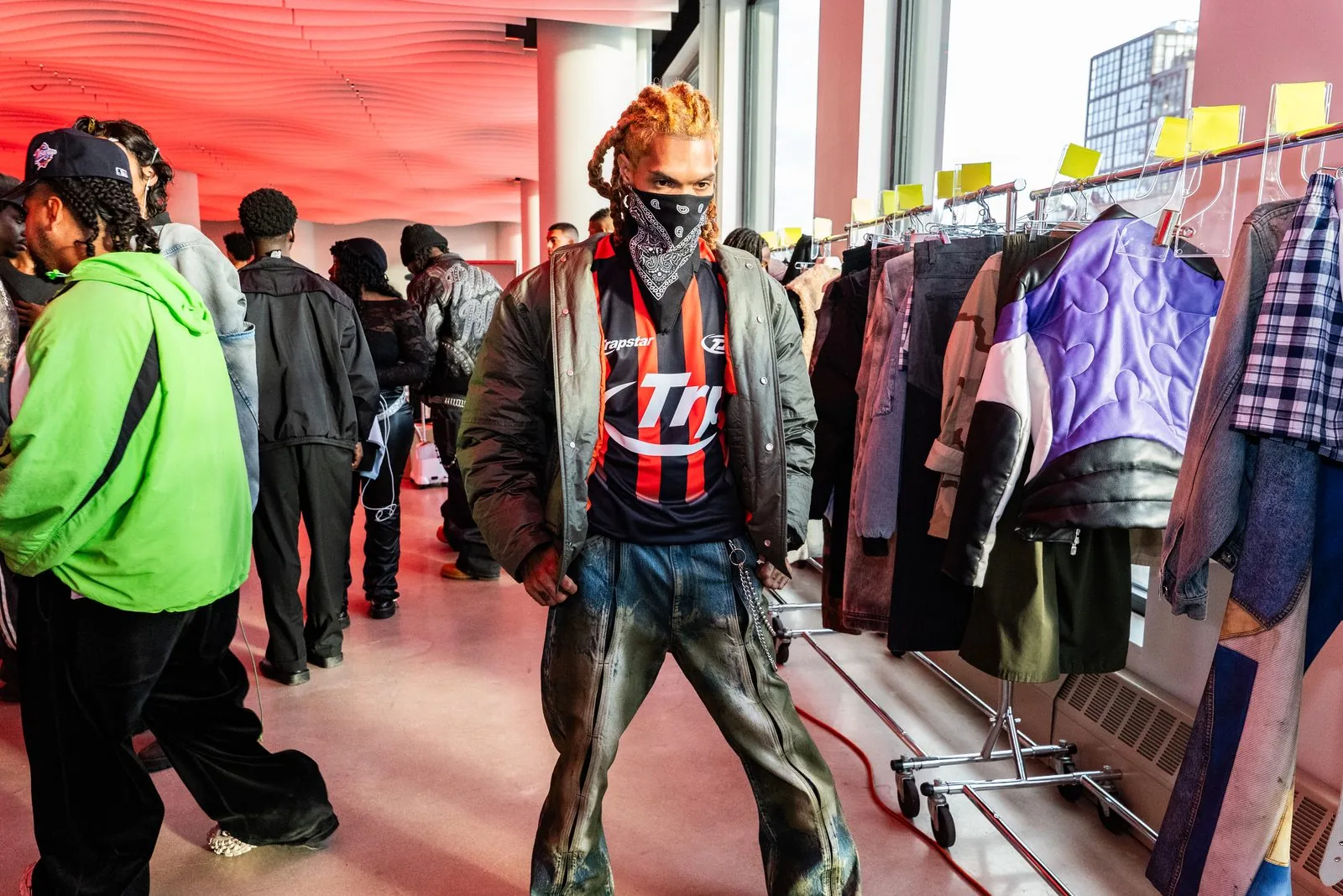 Backstage at the Trapstar London fashion show at VESPER in Brooklyn with a model in streetwear standing beside garment racks