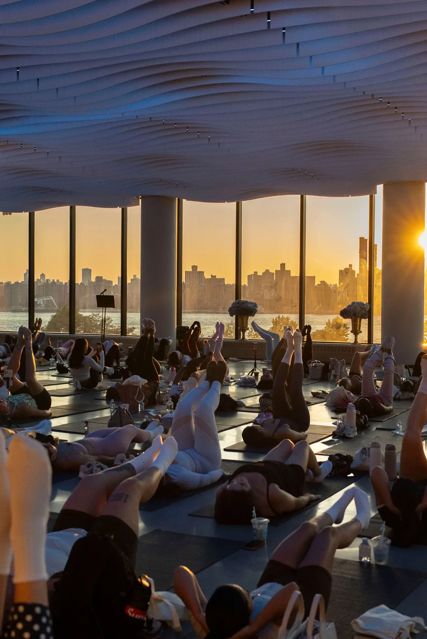 A 120-person mat class at VESPER at golden hour with the Manhattan skyline through the windows in Brooklyn