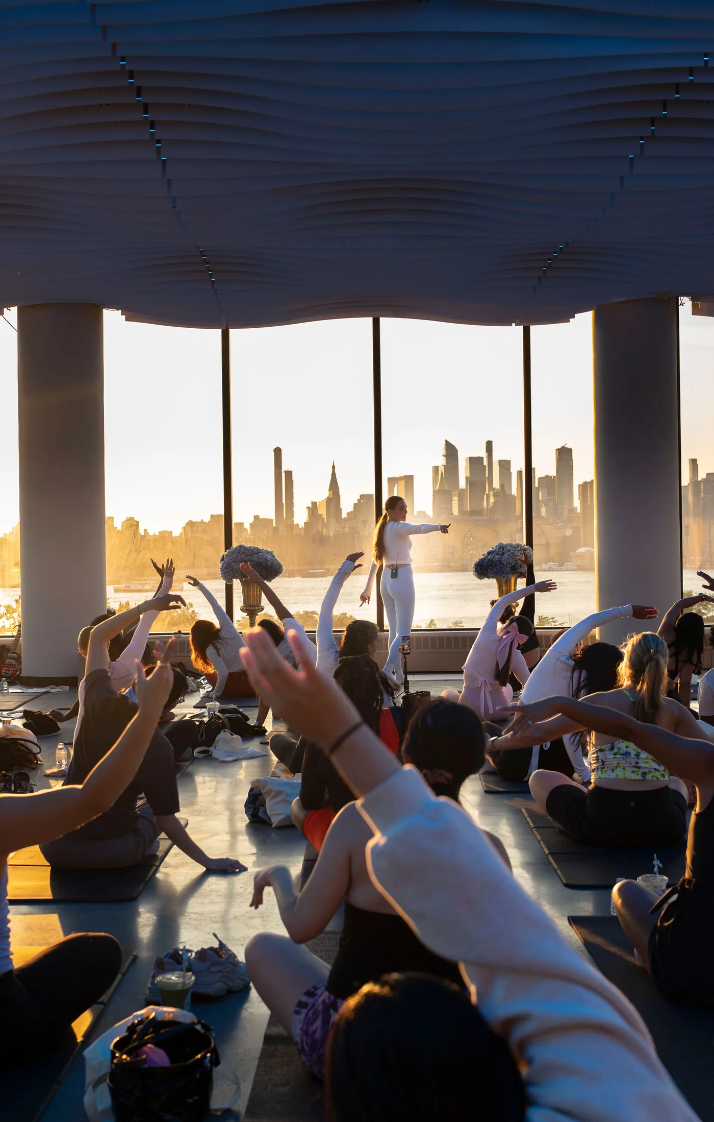 An instructor leading a mat pilates class at VESPER with the class following along and the Brooklyn skyline behind