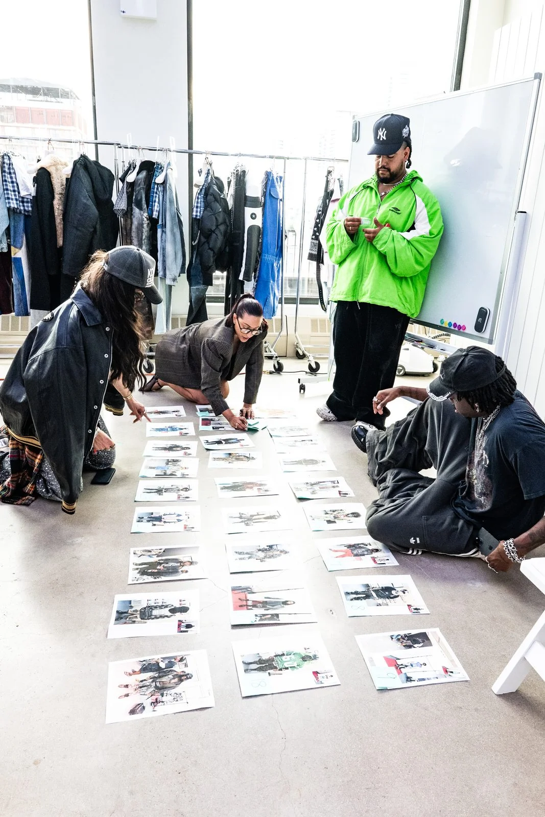 The production team reviewing the run of show on printed look sheets backstage at VESPER, with garment racks and the Manhattan skyline behind them
