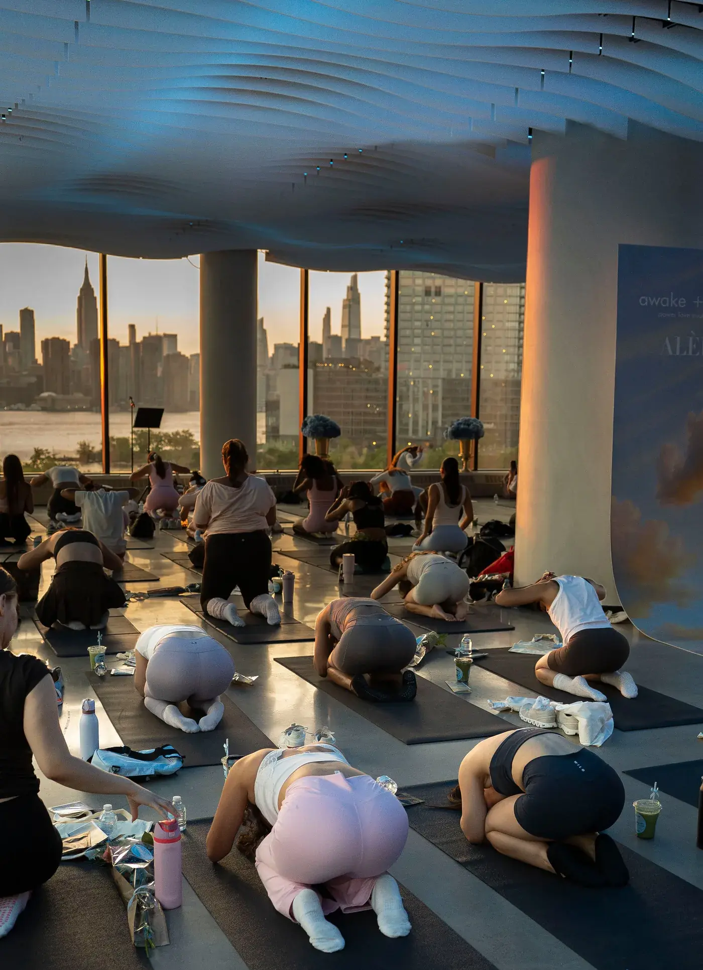 A wellness class resting in child's pose at VESPER with the Manhattan skyline visible through the windows in Brooklyn