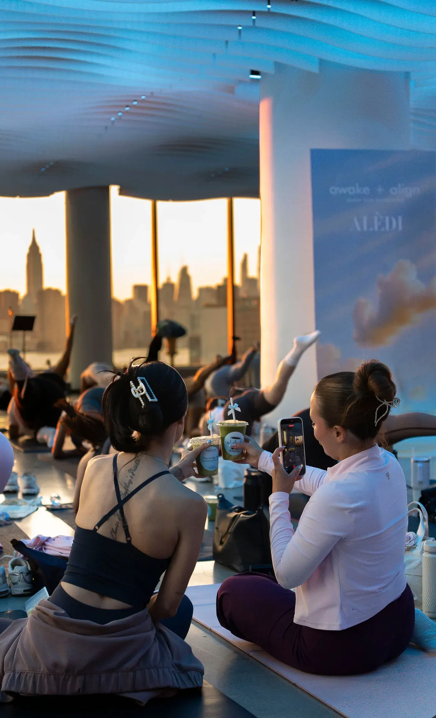 Guests at a VESPER wellness event holding drinks in front of a sponsor's branded backdrop, a vendor activation on the venue floor in Brooklyn