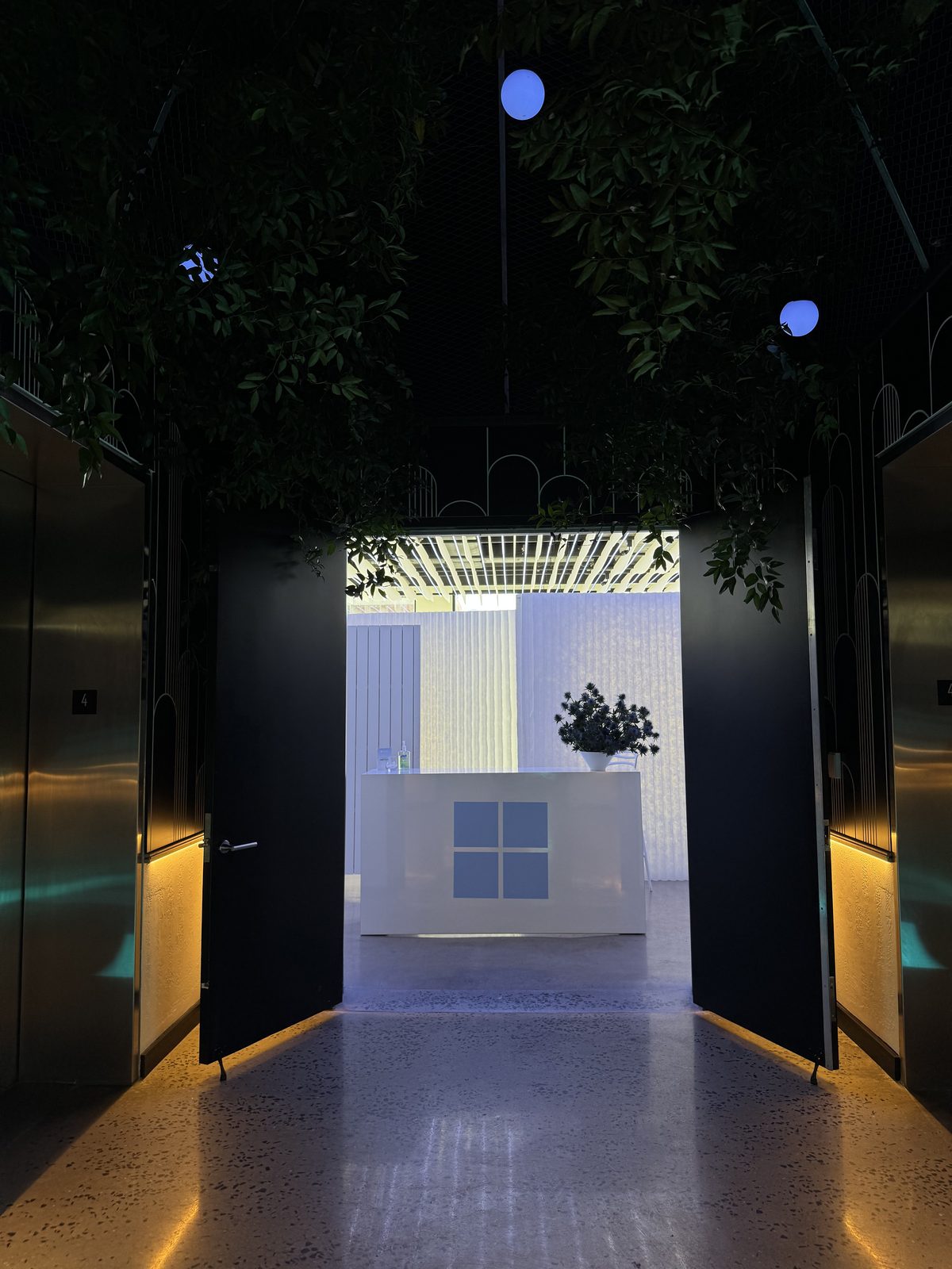 A greenery-covered hallway leading to a Windows-branded check-in counter at VESPER